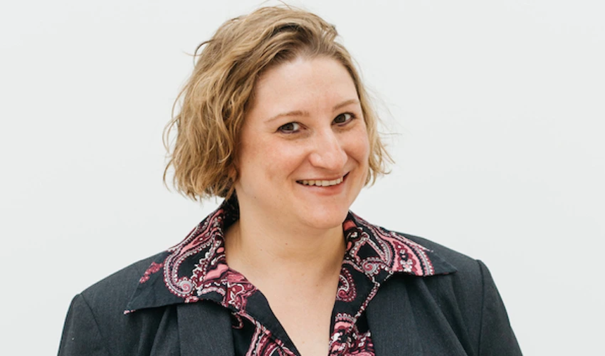 photo of a smiling, short haired white woman wearing a colorful shirt and dark jacket